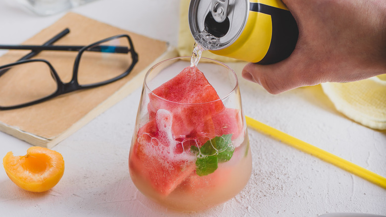 A person pours a canned cocktail into a glass
