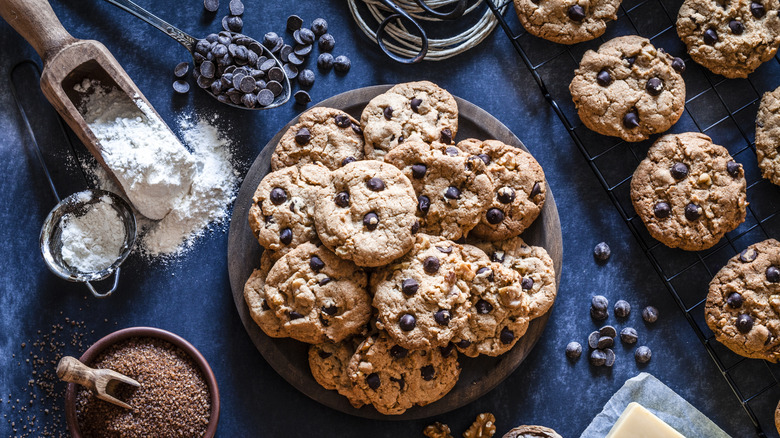Plate of chocolate chip cookies surrounded by baking ingredients and cookie rack