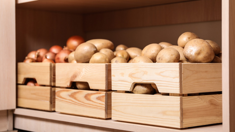 Crates with potatoes and onions are stored orderly on a shelf.