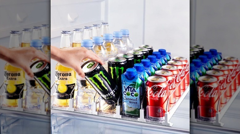 Hand grabbing drink from beverage organizer in fridge.