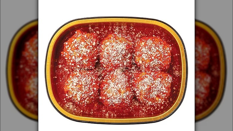 Six meatballs with tomato sauce in a black and gold plastic container on a white background