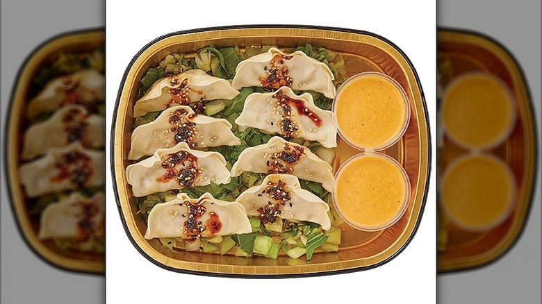 Eight chicken dumplings resting on a bed of lettuce with soy sauce and sesame seeds on top and sauce on the side
