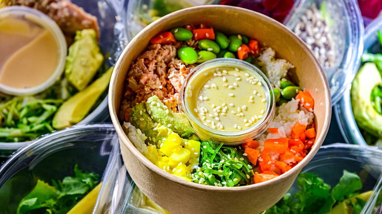 A packaged meal in a paper bowl on top of other prepared meals