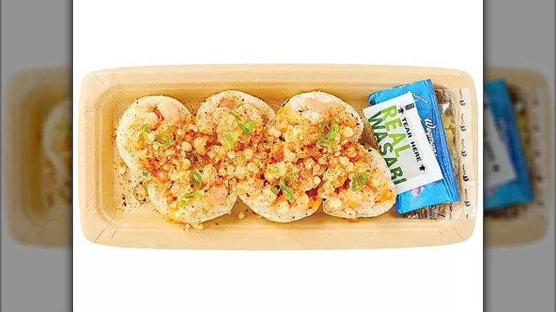 Six sushi pieces with toppings in a disposable container and a packet of wasabi on the side