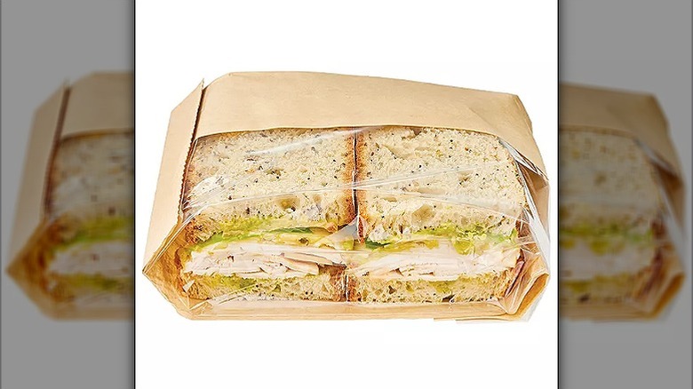 Two halves of a turkey and avocado sandwich in a brown paper bag with transparent sides