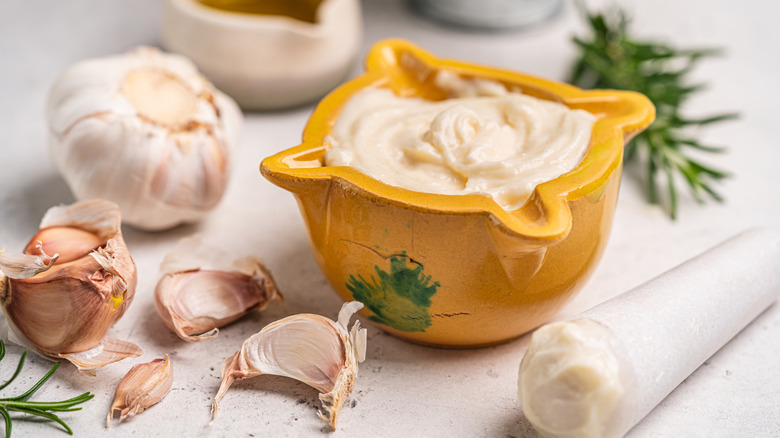A bowl of homemade aioli, surrounded by garlic cloves