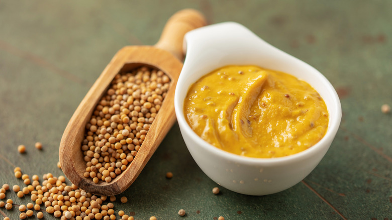 Mustard in a bowl, next to some mustard seeds in a scoop