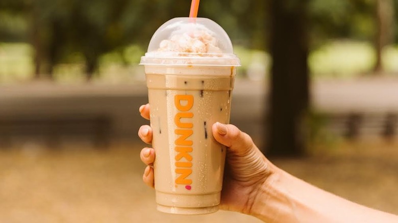 Hand holding a Dunkin' iced coffee with whipped cream