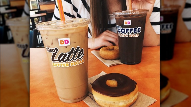 A butter Pecan iced latte in a plastic cup, with a donut