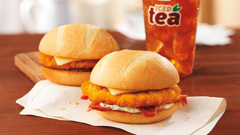 Dunkin' chicken sandwiches on a wooden table in front of a cup of iced tea