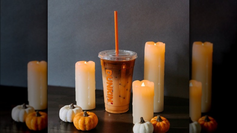 Iced coffee in a Dunkin' takeout cup, surrounded by Halloween candles and pumpkins