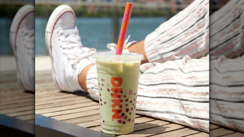 A Dunkin' takeout cup with a drink full of boba pearls, next to someone sitting outside