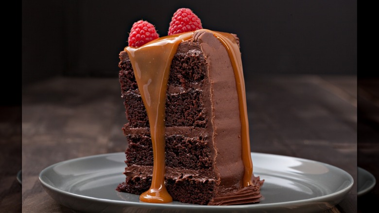A slice of chocolate cake topped with caramel and raspberries, served on a silver plate