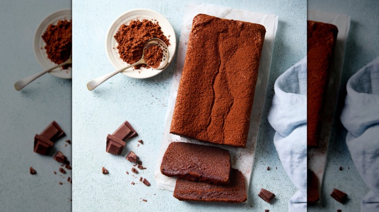 A chocolate loaf cake dusted with cocoa powder on a cutting board