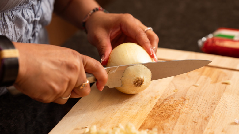 A woman's hands slicing an onion on a cutting board