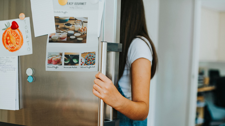 Woman looking inside fridge with hand on door handle