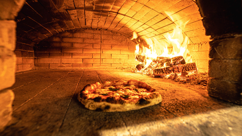 pizza in a brick oven next to a fire