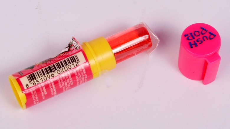 An opened red Push Pop candy next to a branded cap