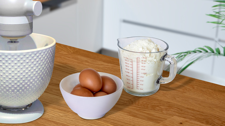 Measuring cup with flour, eggs, mixer