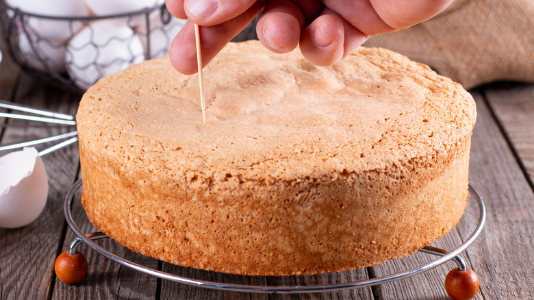 Hand inserting a toothpick into the center of a cake