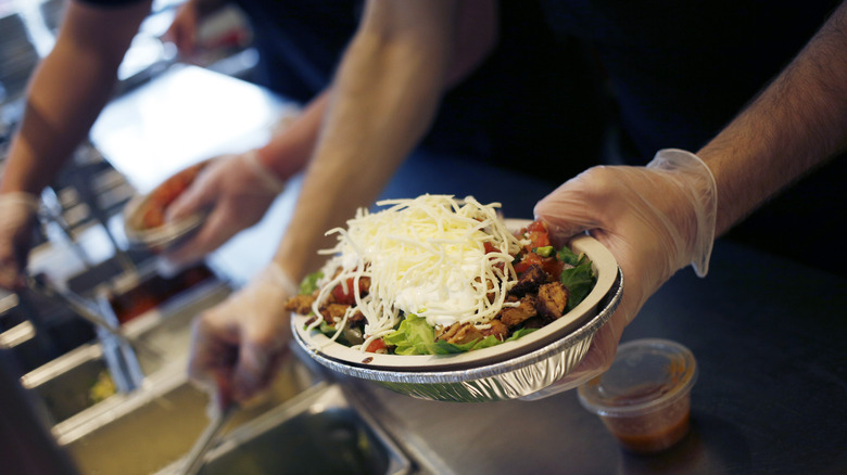 Chipotle workers prepares a bowl topped with cheese
