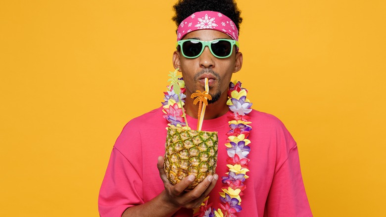 A man in colorful clothing drinks out of a pineapple