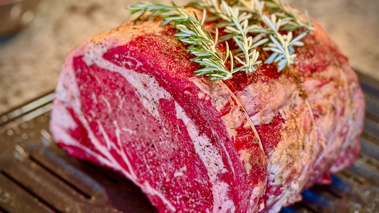 raw rib roast tied up with seasoning on a metal cooking sheet