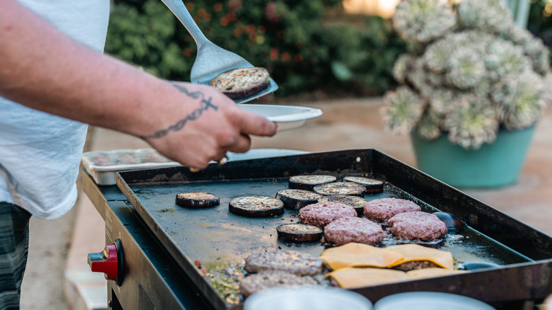 Man serving himself from a flat top grill full of burgers