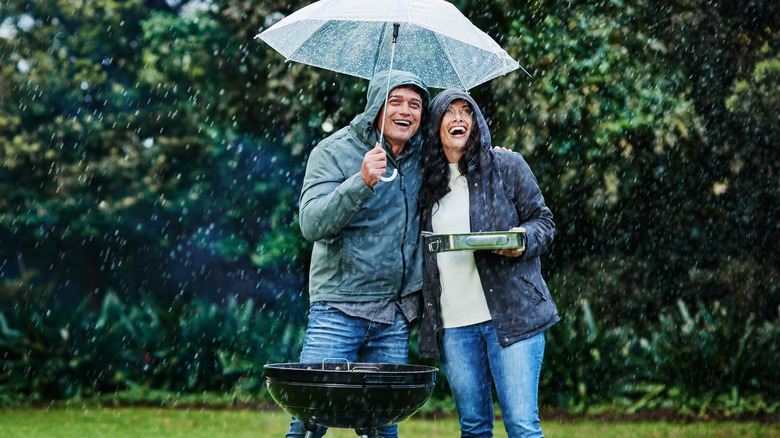couple with umbrella grilling in rain