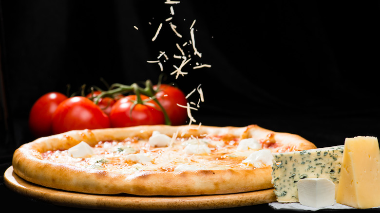 Person sprinkling shredded cheese on pizza