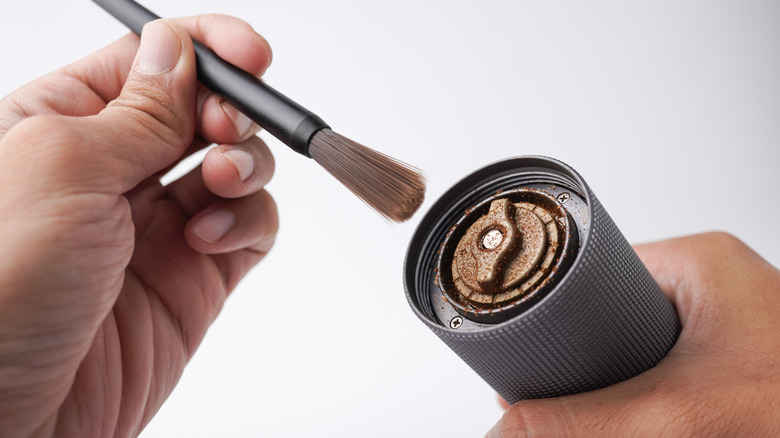 Close up of a hand cleaning a hand grinder with a small brush.