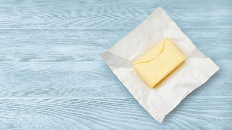 Unwrapped stick of butter, sitting on blue wooden table