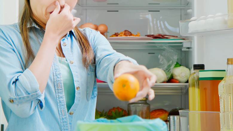 Woman cleaning out her fridge holding stinky fruit