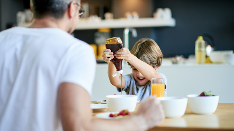 A child squeezing syrup at the breakfast table