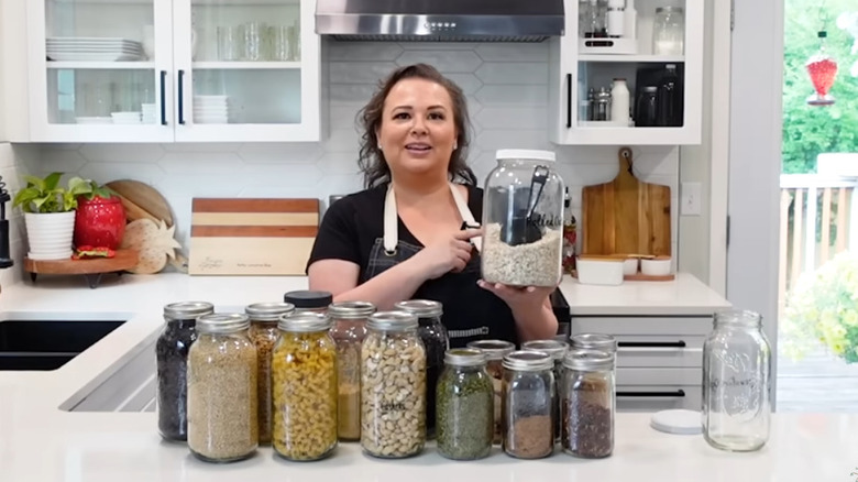 A woman holding a jar of oats with various pantry items in upcycled condiment jars