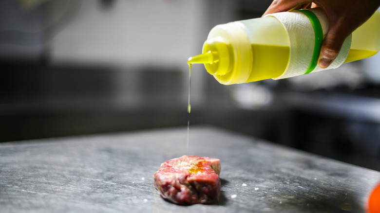 A chef squeezing oil from a bottle onto a steak