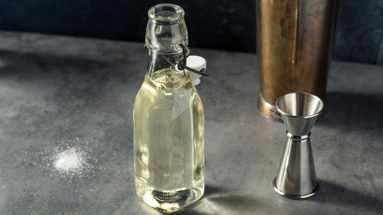 A glass bottle of simple syrup next to a jigger
