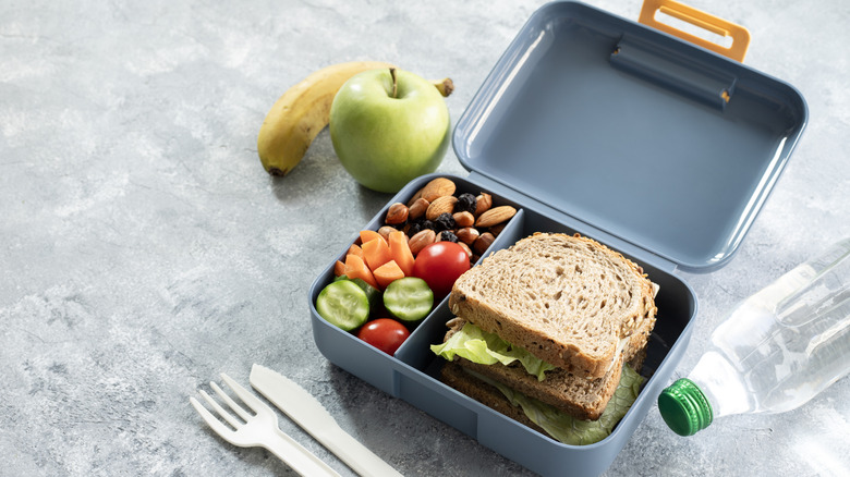 A school lunch box, with sandwiches, sliced vegetables, nuts, and fruit