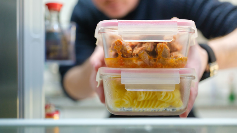 A man takes leftovers in plastic boxes from a fridge