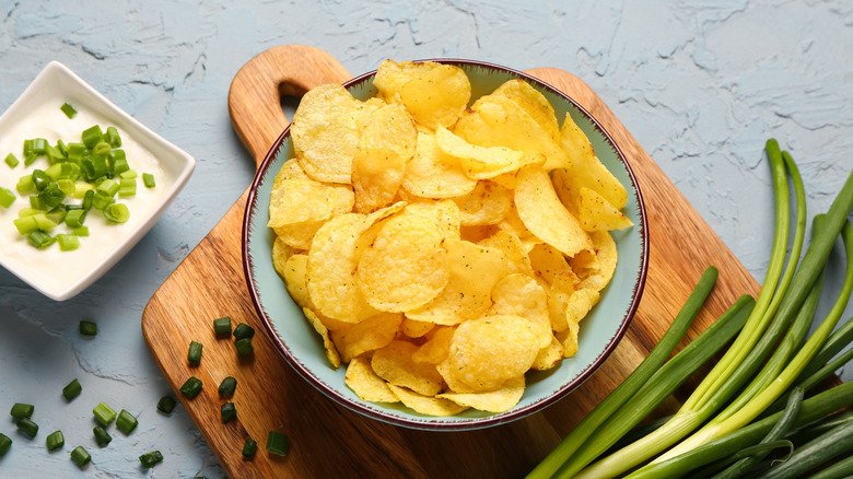 A bowl of sour cream and onion chips, with a bowl of sour cream and green onions next to it