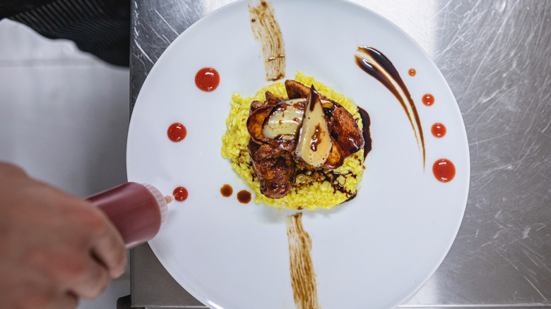 Decorating a white plate with a squeeze bottle of sauce.