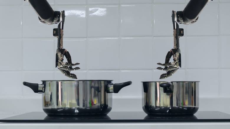 Robotic humanoid hands stirring two large pots of food