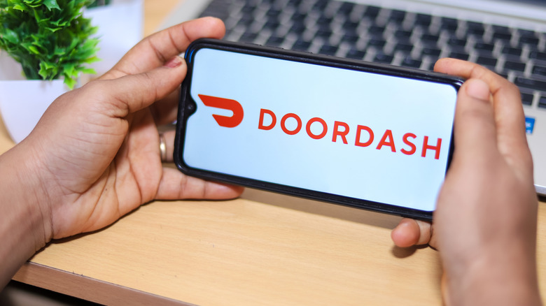 A pair of hands holding a phone that displays the Doordash logo