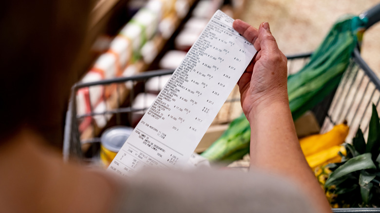 Woman looking at her grocery receipt with items in her cart