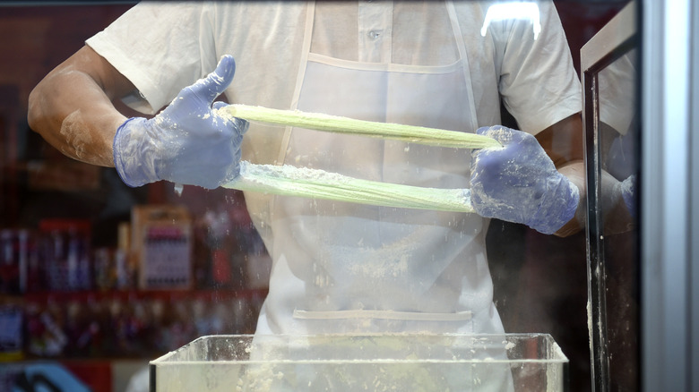 a chef makes dragon's beard candy by pulling threads of sugar over a container filled with flour