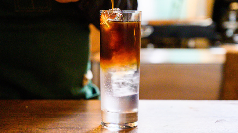 A person pouring coffee into tonic water