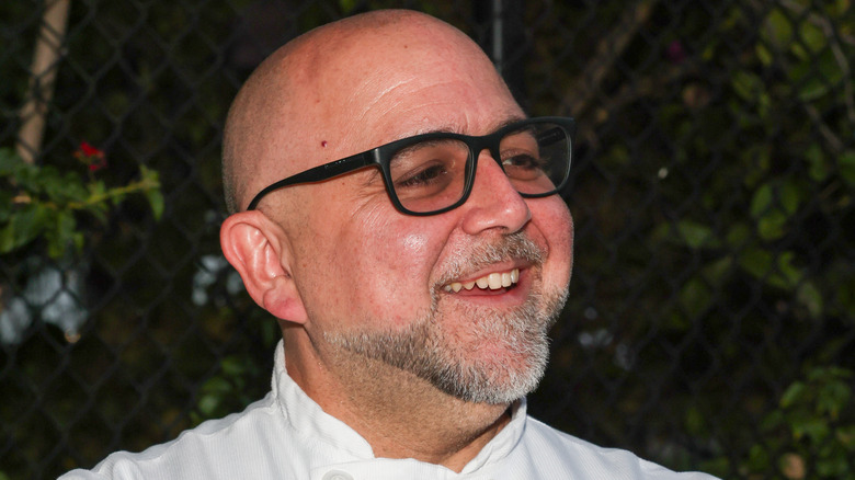 Duff Goldman in chef's whites and black glasses against a fence and greenery.