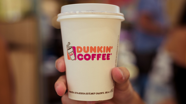 A person holds a paper cup from Dunkin' Donuts