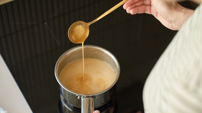 A hand spooning caramel that is cooking in an aluminum saucepan