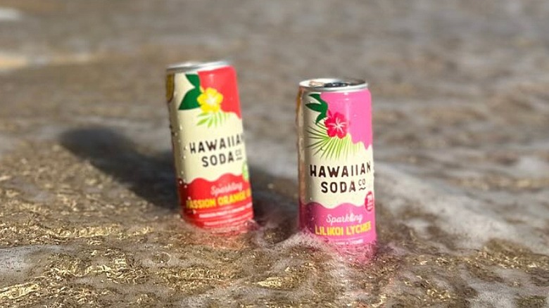 Cans of Hawaiian Soda Co. sodas in the sand on the beach